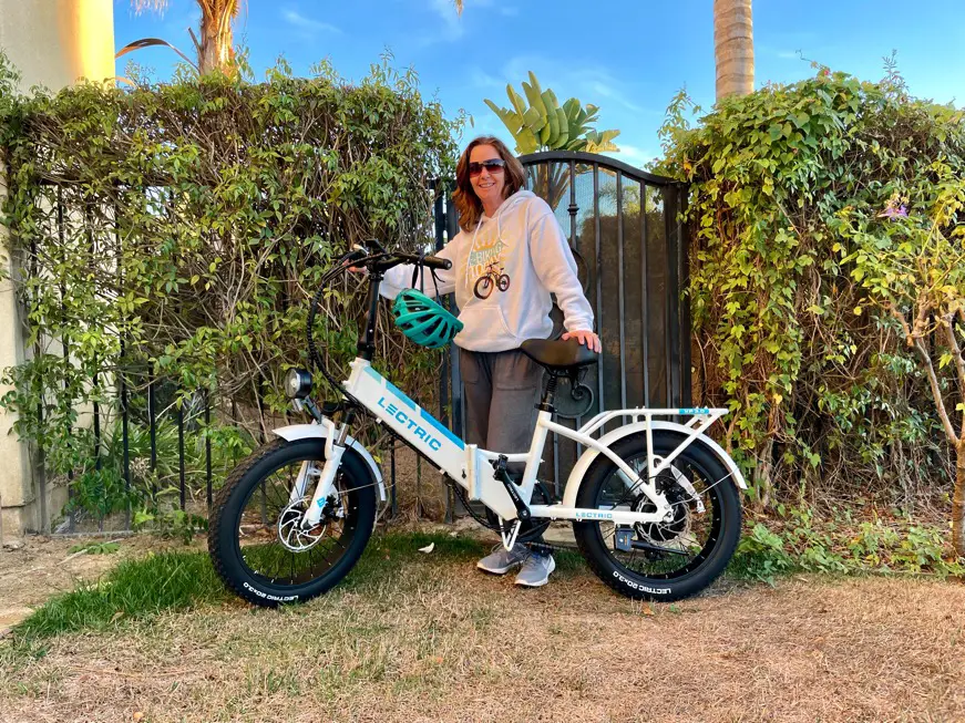 Woman in white sweatshirt standing next to white Lectric e-bike